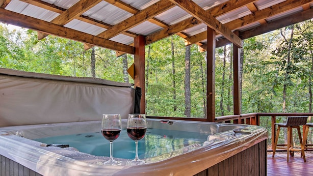 A hot tub with two glasses of red wine, surrounded by wooden deck and trees. - Broken Bow Cabin w/ Hot Tub, Near Hiking + Fishing (Broken Bow)