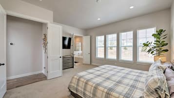 A bedroom with a bed, a dresser, a television, and a window with blinds.