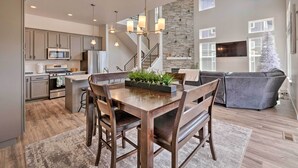 A modern kitchen with grey cabinets, a central island, and a dining area with a wooden table and chairs. - Inviting Hideout Townhome w/ Balcony & Lake Views! (Heber City)