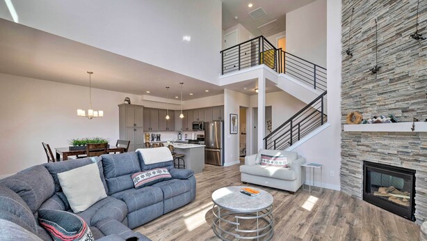 A spacious living area with a gray sectional sofa, a round coffee table, and a stone fireplace. - Inviting Hideout Townhome w/ Balcony & Lake Views! (Heber City)