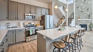 A modern kitchen with grey cabinets, stainless steel appliances, and a large island with bar stools. - Inviting Hideout Townhome w/ Balcony & Lake Views! (Heber City)