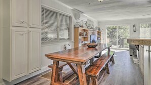 A spacious kitchen with white cabinetry, a wooden dining table, and a large window with blinds. - Furnished Deck & Nat'l Forest Views: Arnold Cabin (Arnold)
