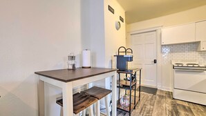 Eine Küche mit weißer Arbeitsplatte, Holzstühlen, einer Kaffeemaschine und einem weißen Kühlschrank.