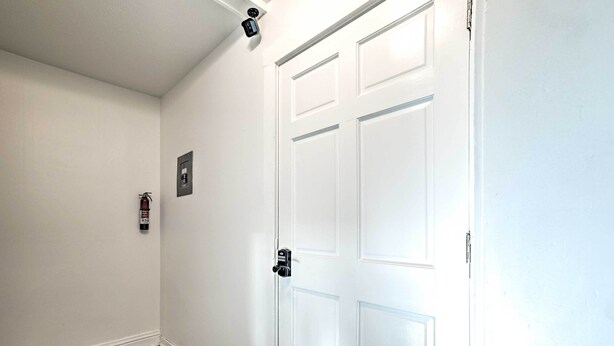 Ein Zimmer mit weißer Tür, einem Rauchmelder und einem Thermostat an der Wand.