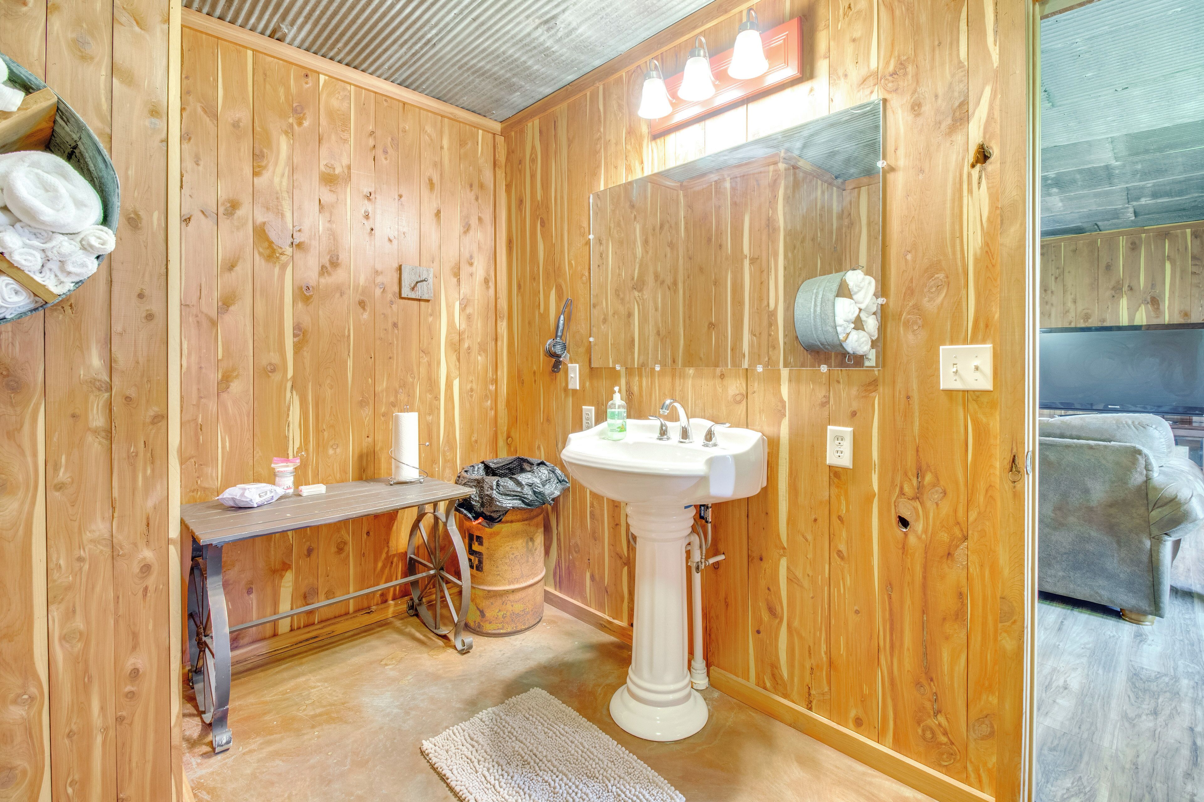 A wooden-paneled bathroom with a sink, mirror, towel rack, and a small table with toiletries.