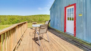 Une terrasse en bois avec une table et des chaises, une porte à cadre rouge et un panneau d’avertissement sur un bâtiment bleu.