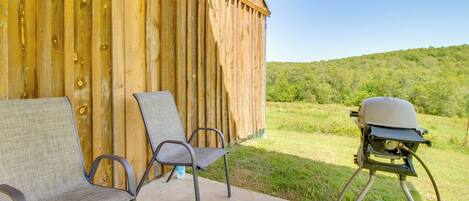 A covered patio with two metal chairs, a barbecue grill, and a propane tank.