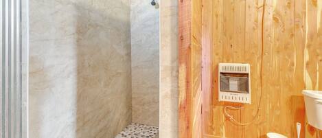 A bathroom with a wooden wall, a shower with a marble floor, and a toilet with a bucket and brush.