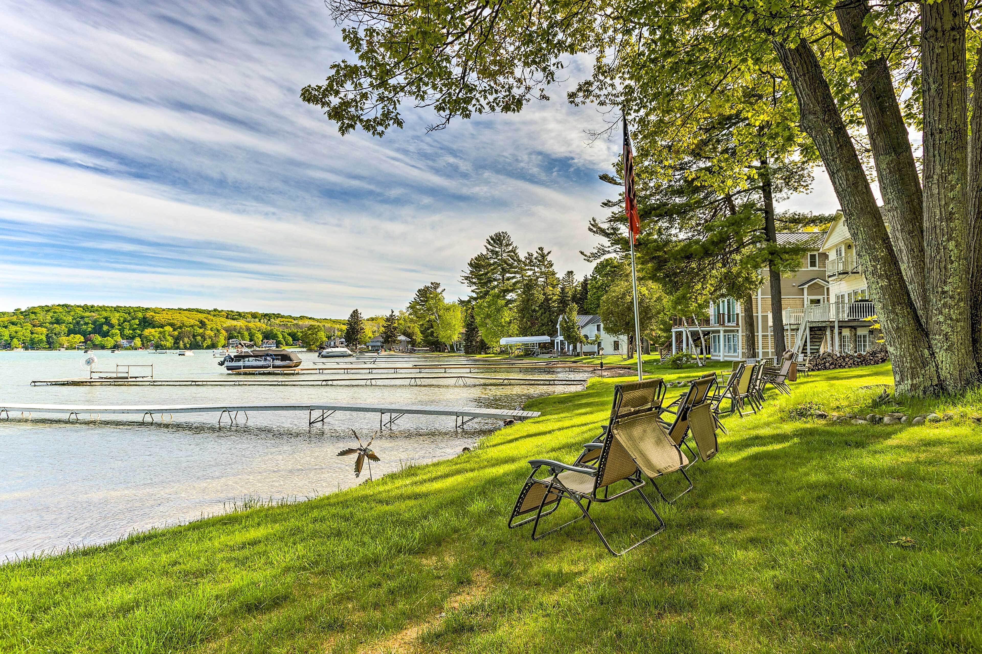 A lakeside view with a dock, boats, and a row of chairs.