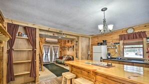 L’intérieur d’un chalet en bois comprend un coin cuisine, des tabourets en bois, une table à manger et un espace de vie chaleureux avec un canapé et une cheminée.