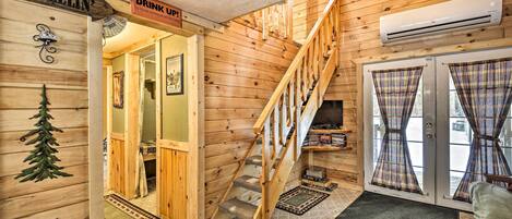 A wooden interior with a staircase, a sign reading "Drink Up!", and a door with plaid curtains.