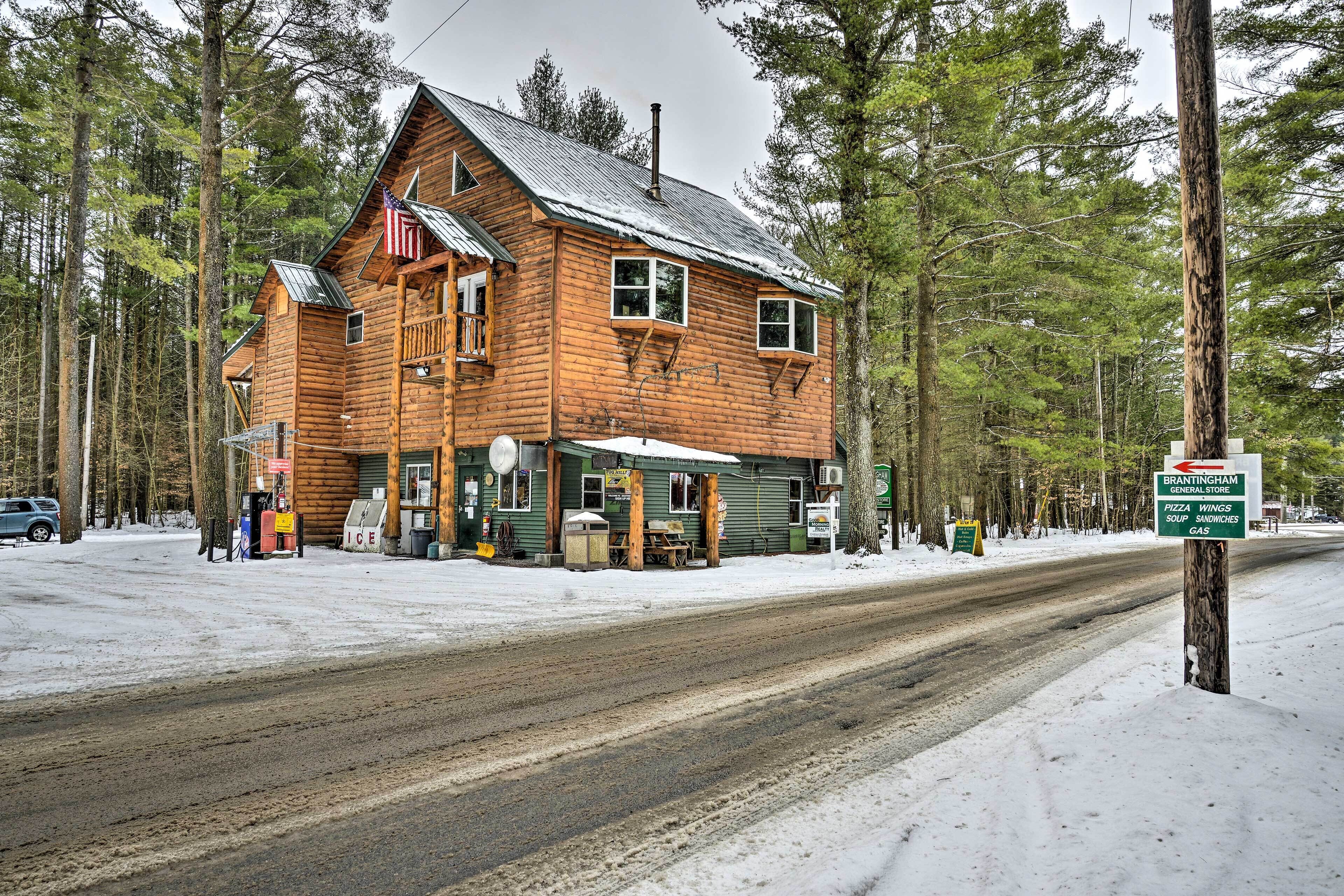 Un bâtiment rustique en bois, sur lequel est accrochée une enseigne publicitaire annonçant une épicerie, des pizzas, des ailes de poulet, des soupes, des sandwichs et de l’essence.