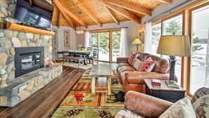A cozy living room with a stone fireplace, leather sofa, and large windows offering a view of the outdoors. - Waterfront Gull Lake w/ Dock: Family Friendly! (Nisswa)