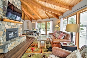 A cozy living room with a stone fireplace, leather sofa, and large windows offering a view of the outdoors.