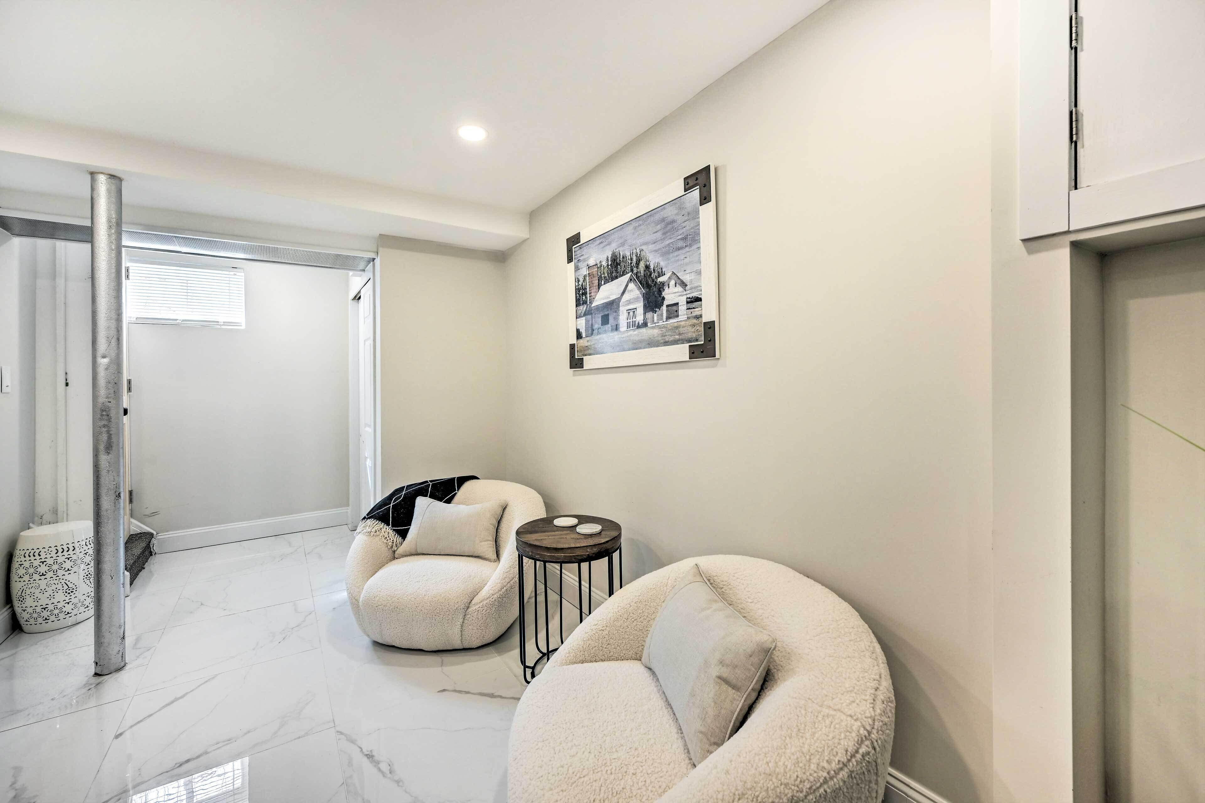 A modern living room with two plush armchairs, a small round table, and a framed picture on the wall.