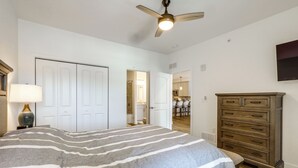 A bedroom with a large bed, a ceiling fan, a dresser, and a view into the kitchen. - Bright Lewes Condo w/ Balcony, 7 Mi to Beach! (Lewes)