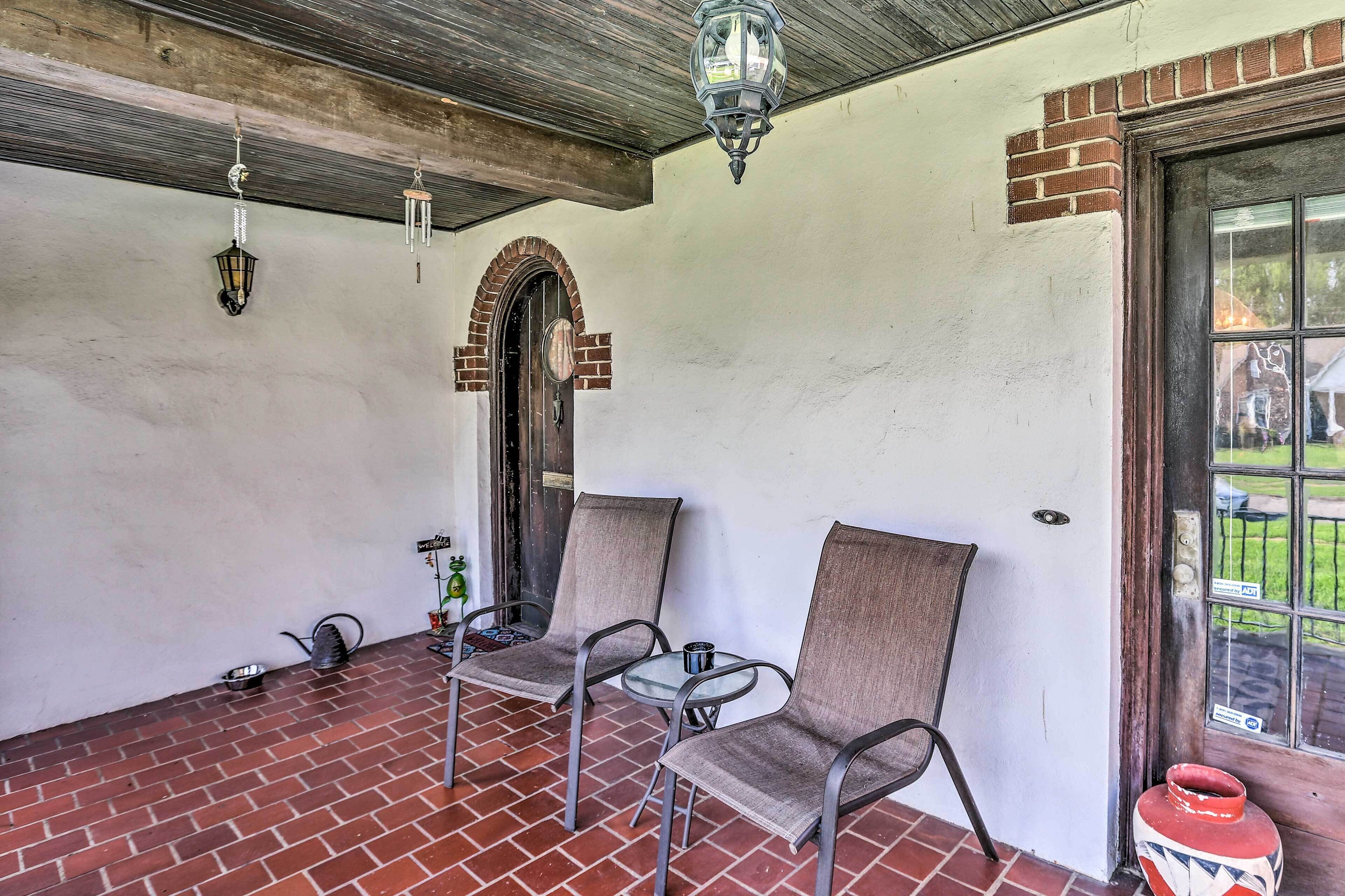 A covered patio area with brick flooring, two metal chairs, a small table, and a hanging lantern.