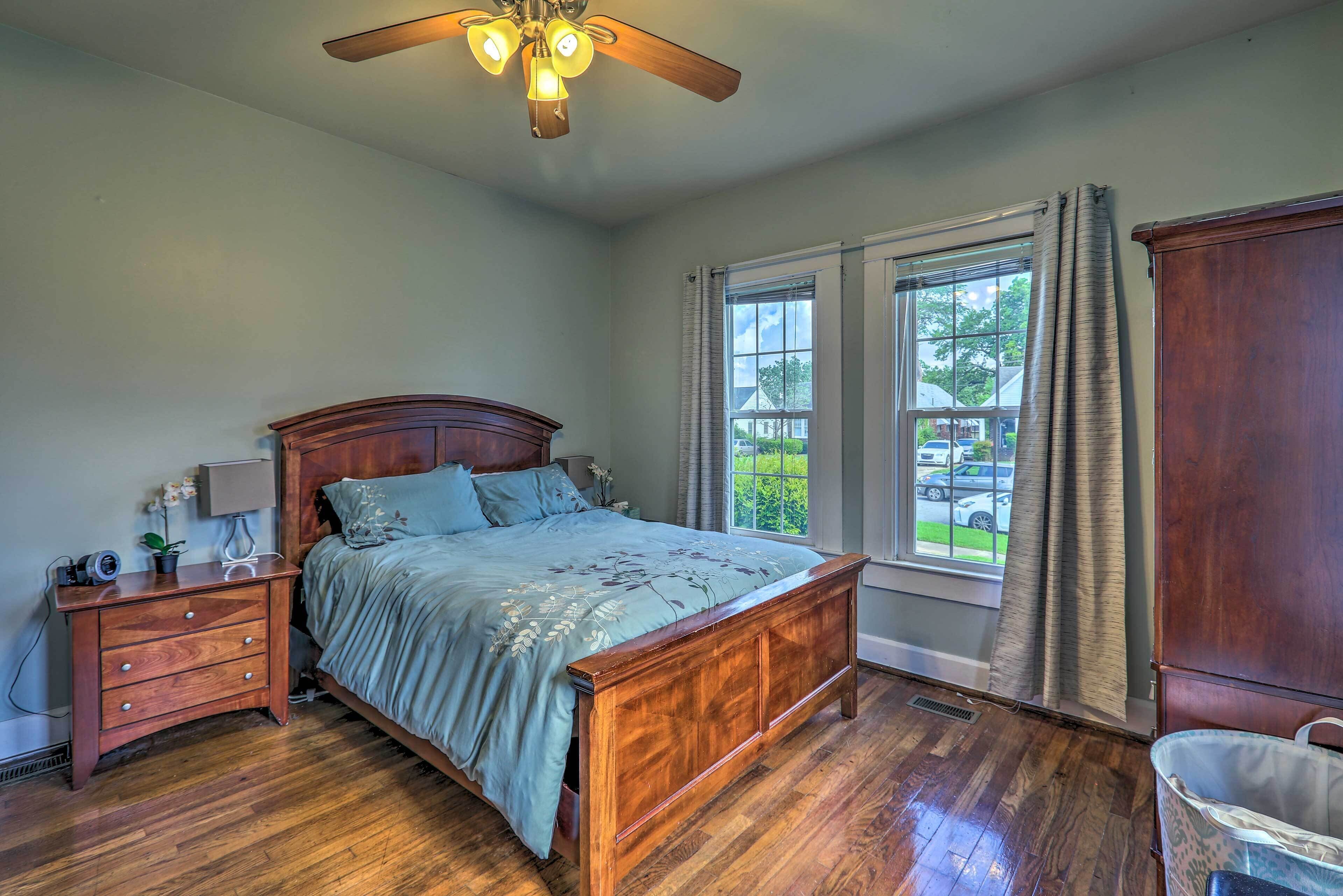 A bedroom with a wooden bed, a nightstand, a ceiling fan, and a window with curtains.