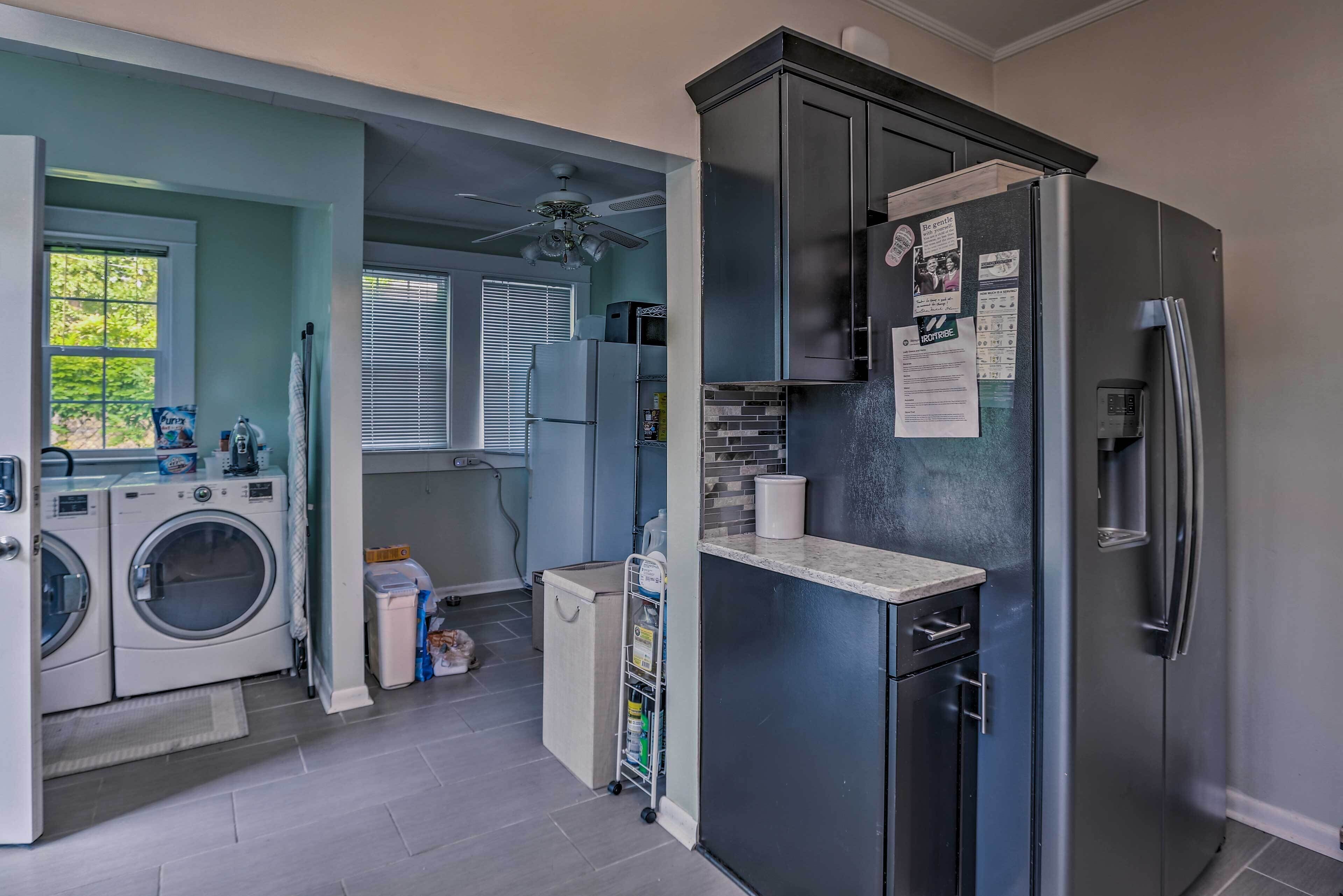 A compact kitchen with a refrigerator, washing machine, and a small utility cart.