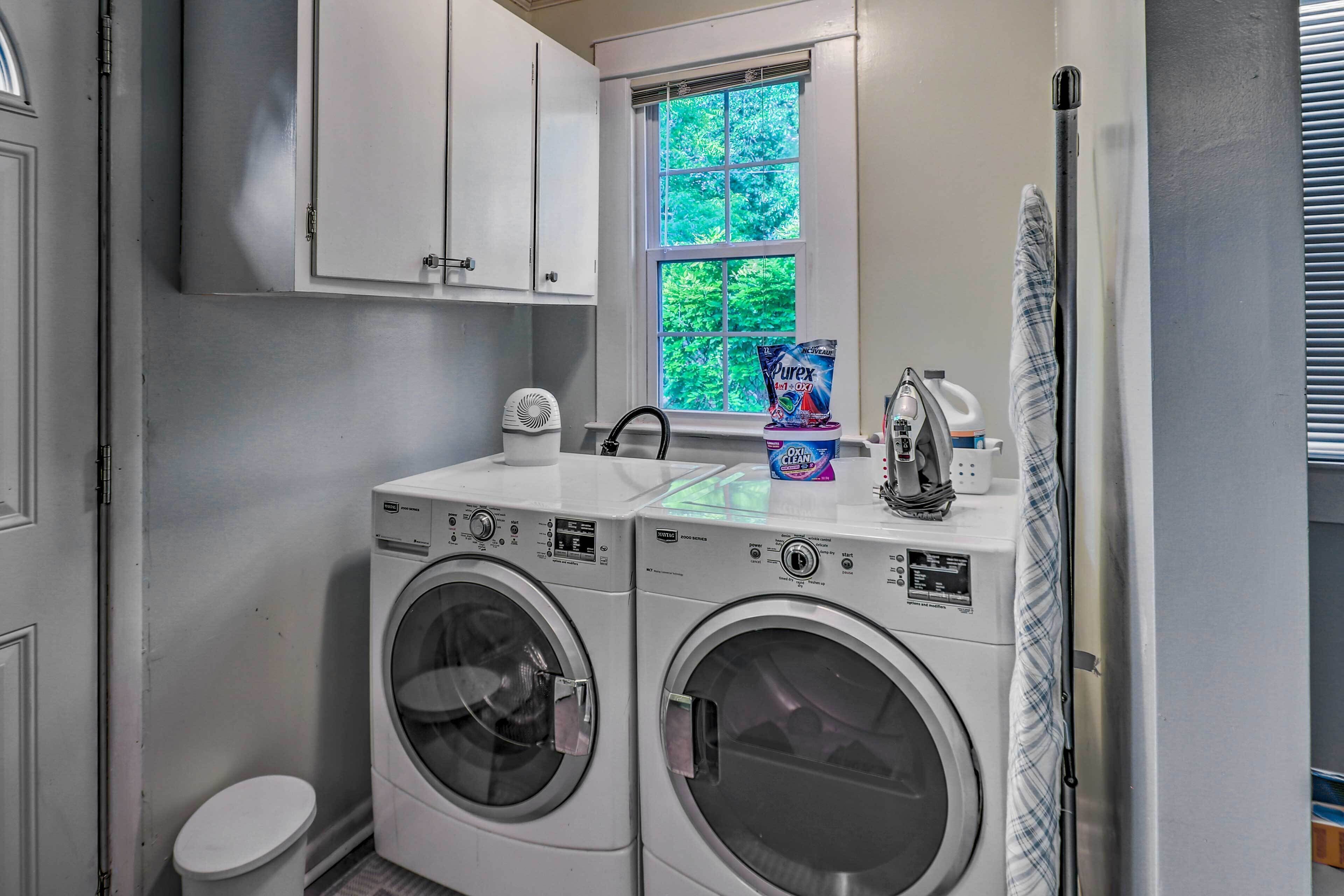A laundry room with two front-loading washing machines, a dryer, and a window with a view of greenery.