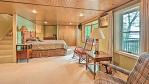 A bedroom with a wooden ceiling, a bed with plaid bedding, a rocking chair, a desk with a lamp, and a window with a view of trees. - 2 Mi to Winery: Le Roy Escape w/ Fire Pit & Views (Le Roy)