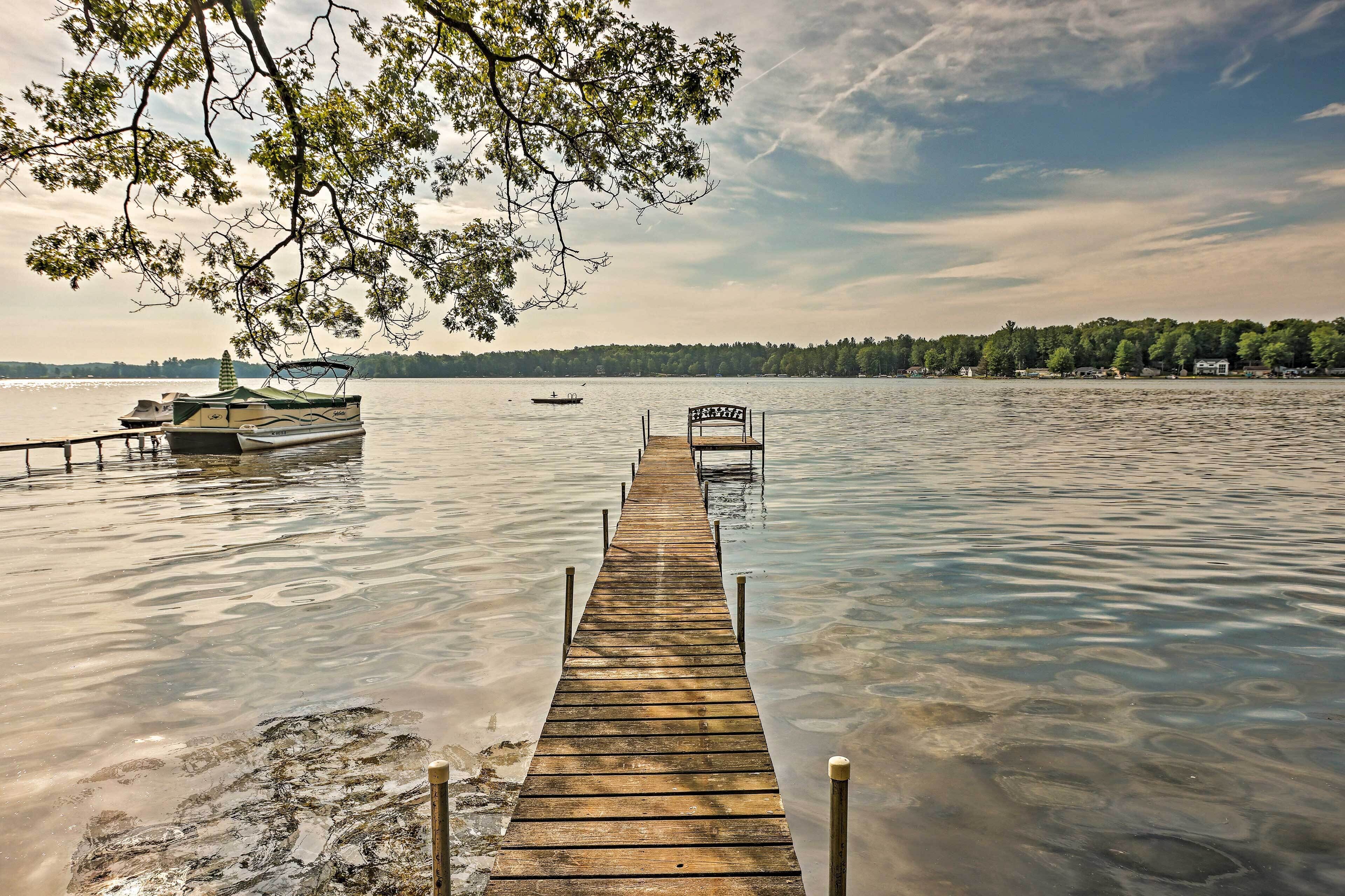 A wooden pier extending into calm water with a bench at the end, surrounded by trees and a distant shoreline.