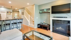 A modern living room with a fireplace, a TV mounted above it, and a kitchen area with bar stools. - Walk to Local Shops & Eats! Quaint Issaquah Home (Issaquah)