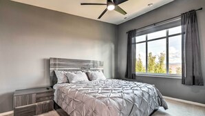A bedroom with a bed, a nightstand, a ceiling fan, and a large window with curtains. - Walk to Local Shops & Eats! Quaint Issaquah Home (Issaquah)
