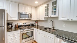 A modern kitchen with white cabinets, stainless steel appliances, a granite countertop, and a built-in dishwasher. - Cape May Quad w/ Grill - 7 Blocks to Beach! (Cape May)
