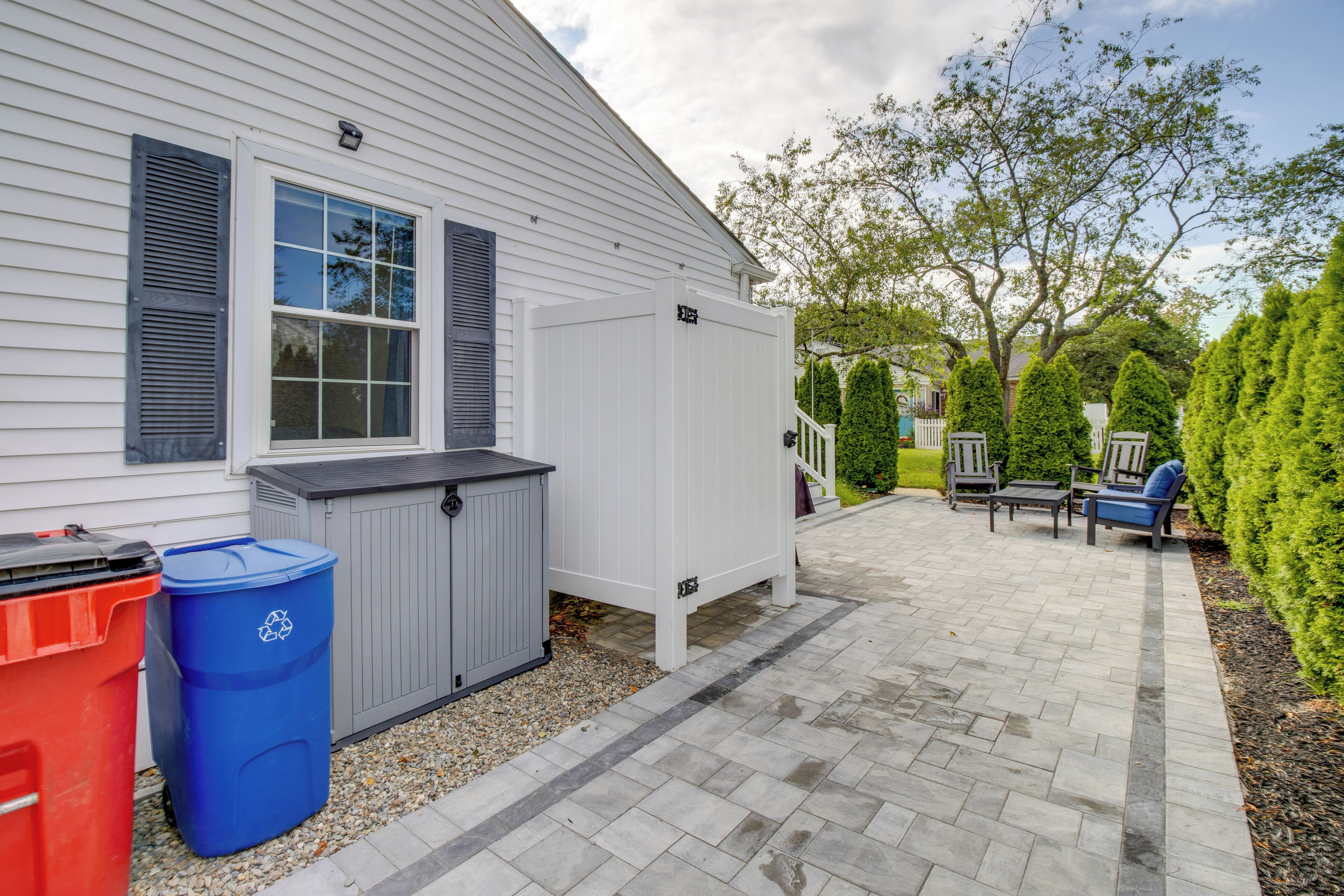 A house with a covered patio area, a trash bin, and a small outdoor seating area with a table and chairs.