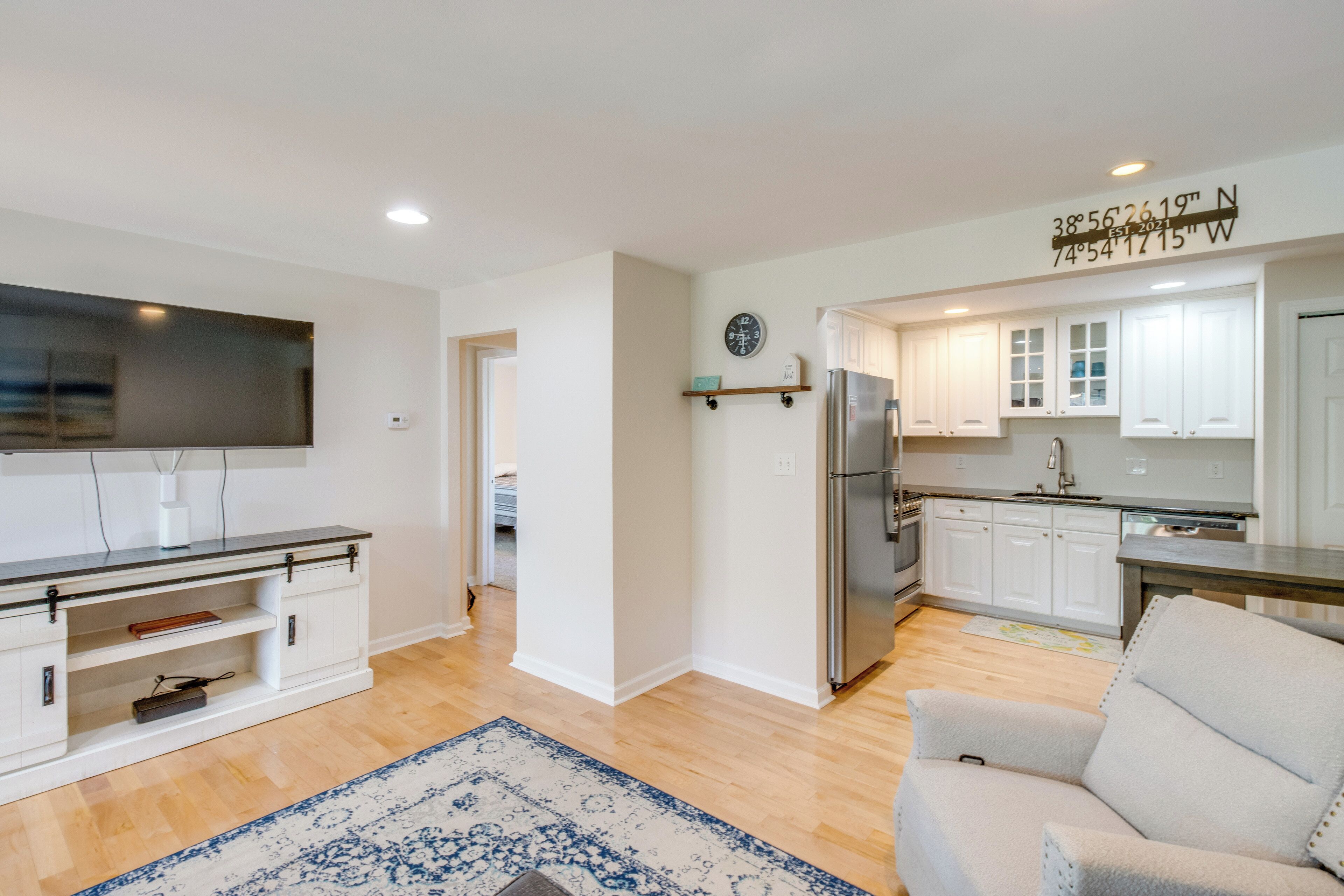 A modern kitchen with white cabinets, a stainless steel refrigerator, and a flat-screen TV mounted on the wall.