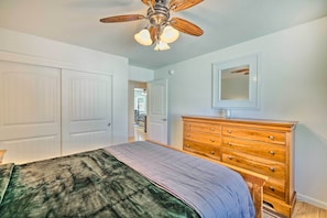 A bedroom with a bed, a wooden dresser, a ceiling fan, and white doors.