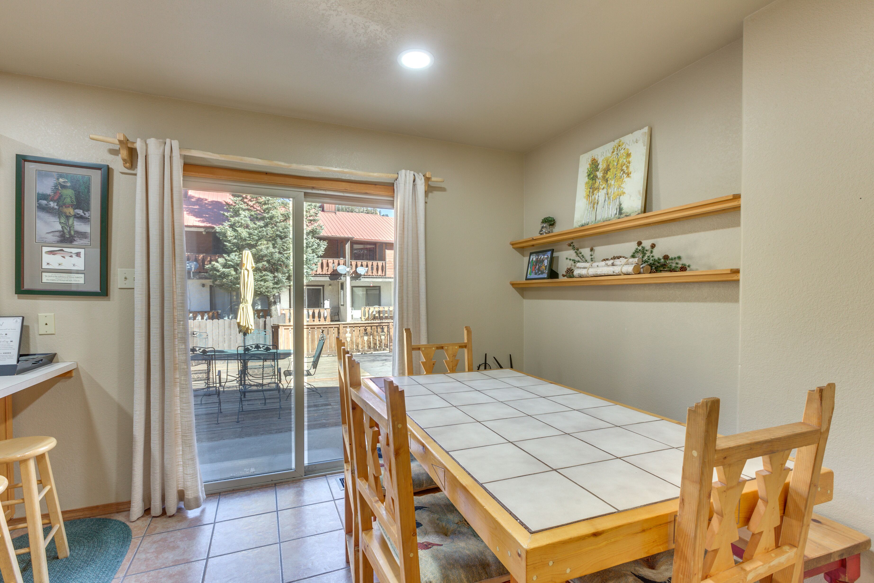 A dining area with a wooden table and chairs, a sliding glass door leading to an outdoor patio, and a small shelf with decorative items.