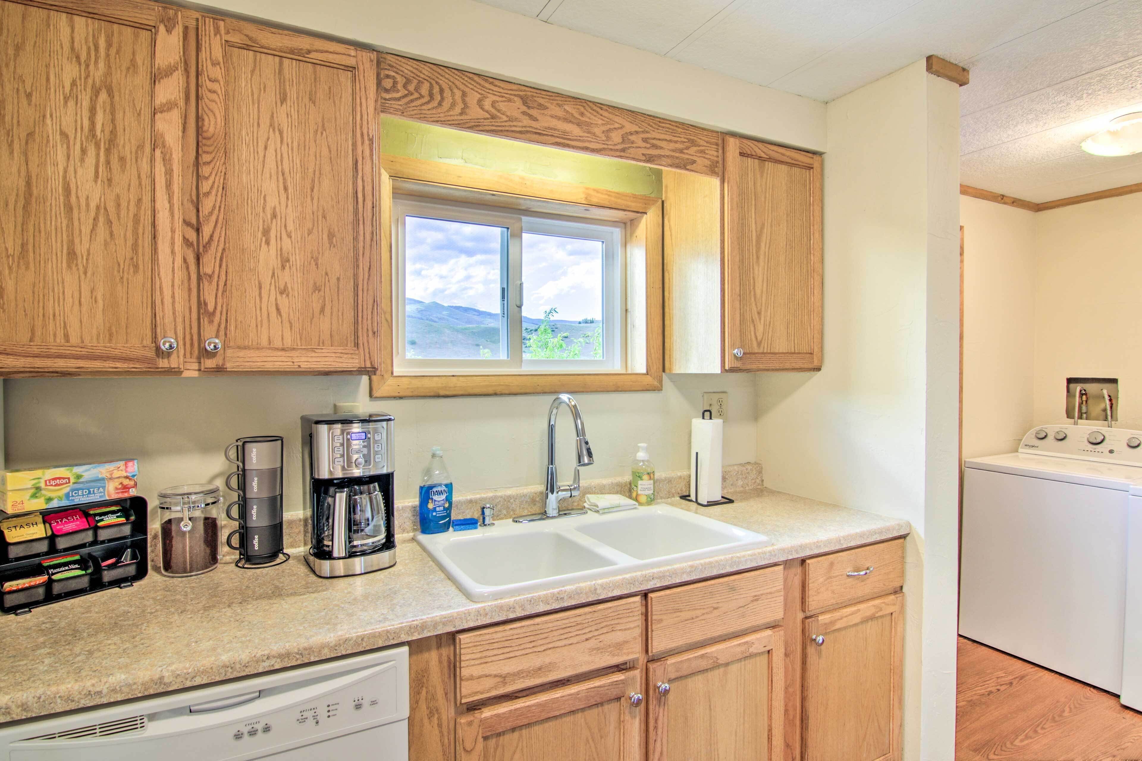 A kitchen with wooden cabinets, a double sink, a coffee maker, a dishwasher, and a window with a view of the outdoors.
