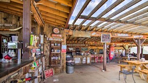 A rustic outdoor seating area with wooden tables and chairs, a bar counter with various bottles, and a dog figurine.