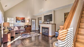 A spacious living room with a fireplace, a television mounted above it, and a staircase leading to an upper level. - Heber Springs Cabin ~ 1 Mi to Sugarloaf Mtn! (Heber Springs)