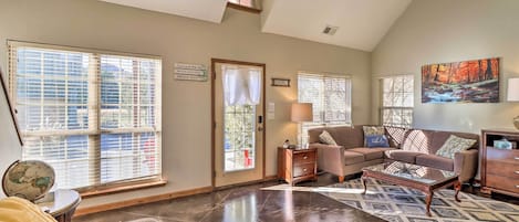 A spacious living room with a high ceiling, large windows, a fireplace, and a cozy seating area.