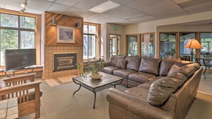A spacious living area with a large leather sofa, a flat-screen TV, a fireplace, and large windows allowing natural light.