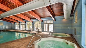 An indoor swimming pool with wooden beams, a jacuzzi, and a tiled wall.