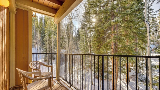 A wooden deck with a railing, overlooking a snowy forest.
