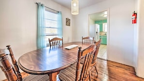 A dining area with a wooden table and chairs, a hanging light fixture, a window with blue curtains, and a kitchen visible through an open door. - Outdoor Dining & Yard: Pet-friendly Temple Home (Temple)