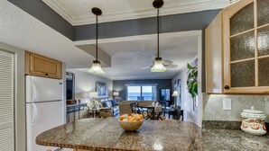 A kitchen with a granite countertop, wooden cabinets, and a bowl of fruit. - Oceanfront- Heated Pool-Balcony (Indialantic)