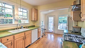 A kitchen with wooden cabinets, a sink, a stove, and a window with a view of greenery. - Colorful Pensacola Oasis: 1 Block to Bayview Park! (Pensacola)