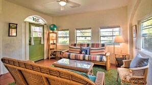 A cozy living room with wicker furniture, a ceiling fan, and large windows. - Colorful Pensacola Oasis: 1 Block to Bayview Park! (Pensacola)