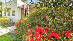 A building with a white exterior, a flag, and a garden with red flowers. - Colorful Pensacola Oasis: 1 Block to Bayview Park! (Pensacola)