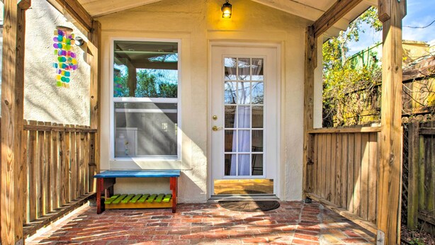 A covered porch with a brick floor, a wooden bench, a white door, and a window. - Colorful Pensacola Oasis: 1 Block to Bayview Park! (Pensacola)
