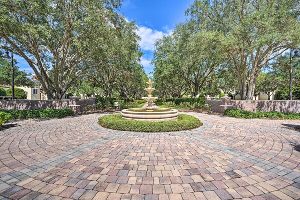 A circular brick pathway with a central fountain, surrounded by trees and a clear sky.