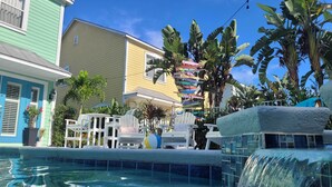 A pool area with a waterfall feature, white lounge chairs, and tropical plants. - 7 Mi to Disney: Reunion Resort Oasis w/ Pool (Kissimmee)