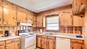 A kitchen with wooden cabinets, a stove, a sink, and a window with blinds. - Charming Aiken Vacation Rental 2 Mi to Dtwn! (Aiken)