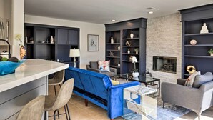 Una sala de estar moderna con un sofá azul, sillones grises, una mesa de centro de vidrio y una chimenea.